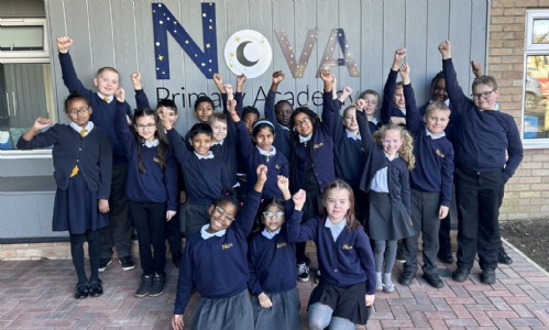 Nova Primary students outside of the Nova Primary Academy Logo with arms in the air, smiling to celebrate good Ofsted result.